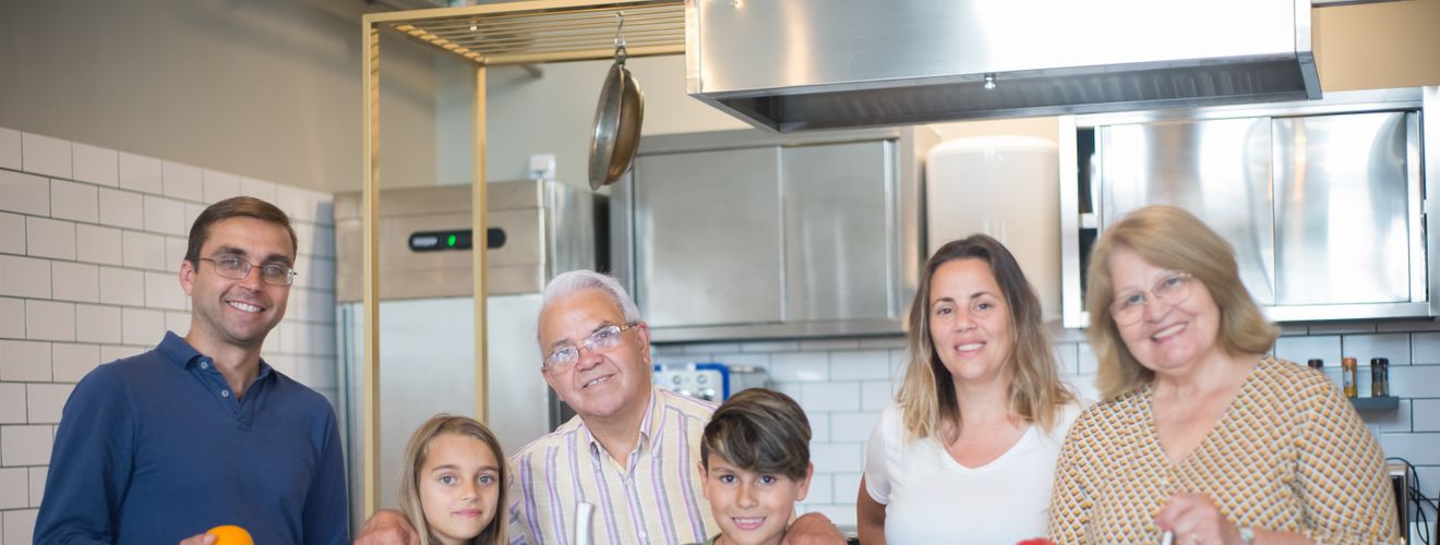 A family of six smiling while preparing food in a modern kitchen.