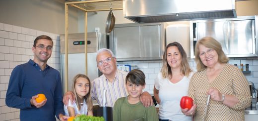 A family of six smiling while preparing food in a modern kitchen.
