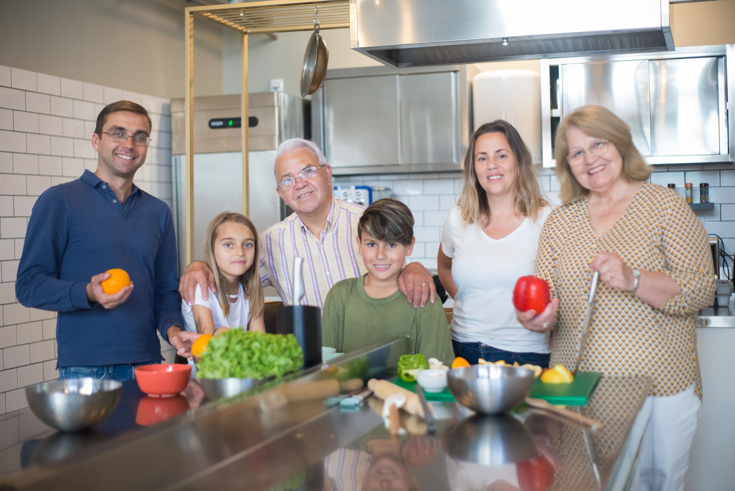 A family of six smiling while preparing food in a modern kitchen.