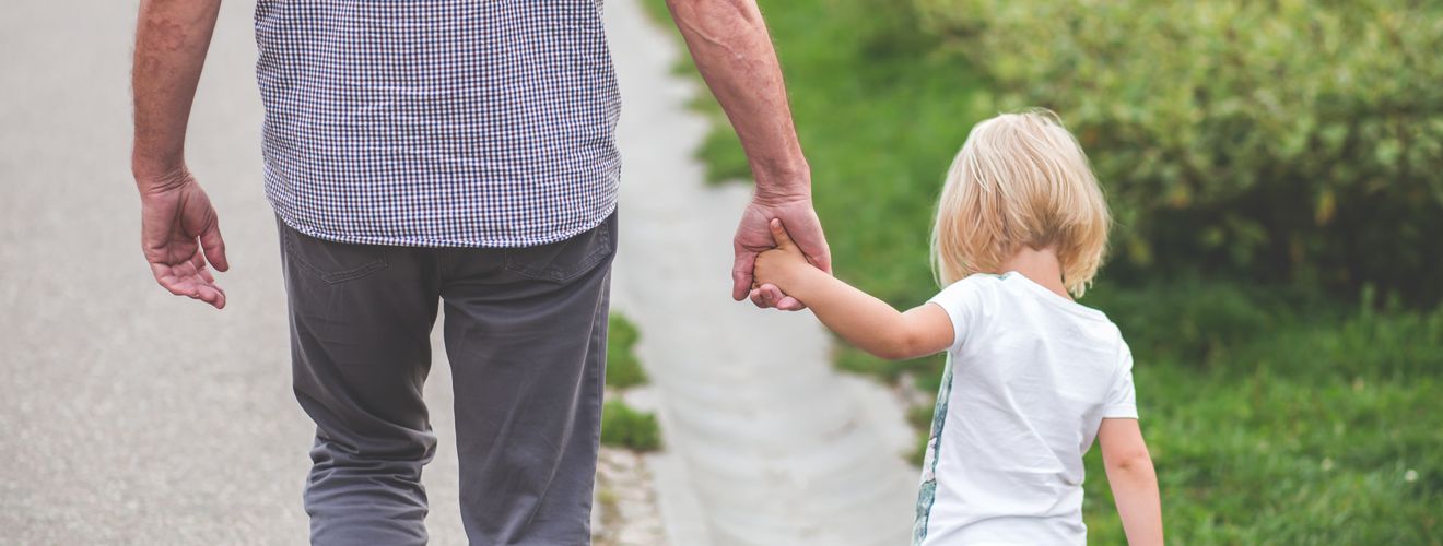 A grandparent holds hands with a child, walking on a path in a park, symbolizing family and togetherness.