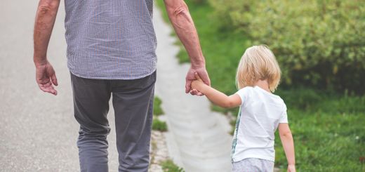 A grandparent holds hands with a child, walking on a path in a park, symbolizing family and togetherness.