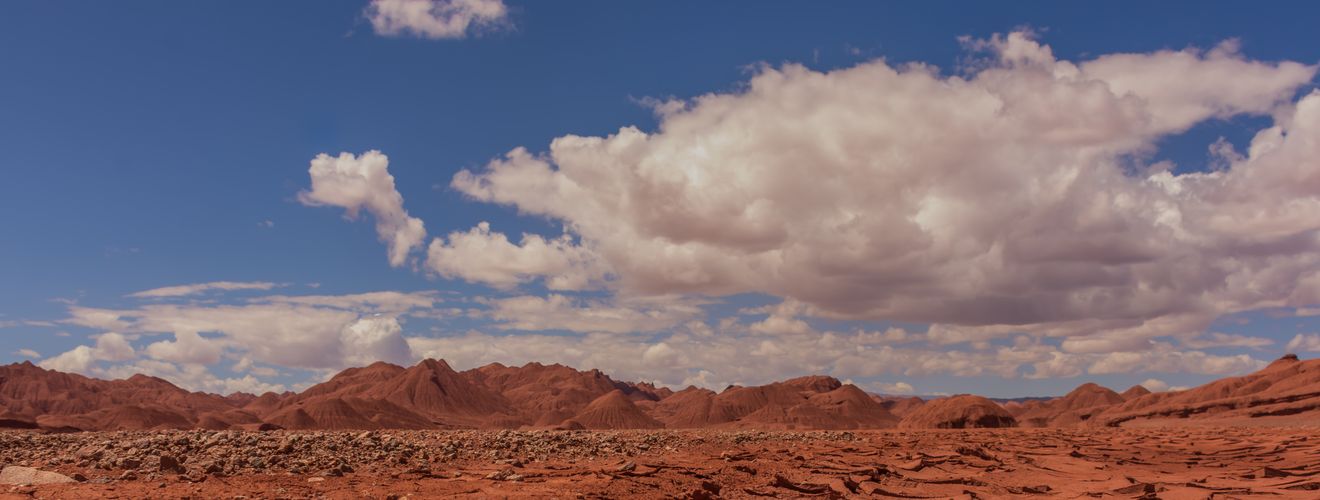 A stunning view of a cracked red desert under a bright blue sky with scattered clouds.