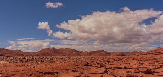 A stunning view of a cracked red desert under a bright blue sky with scattered clouds.