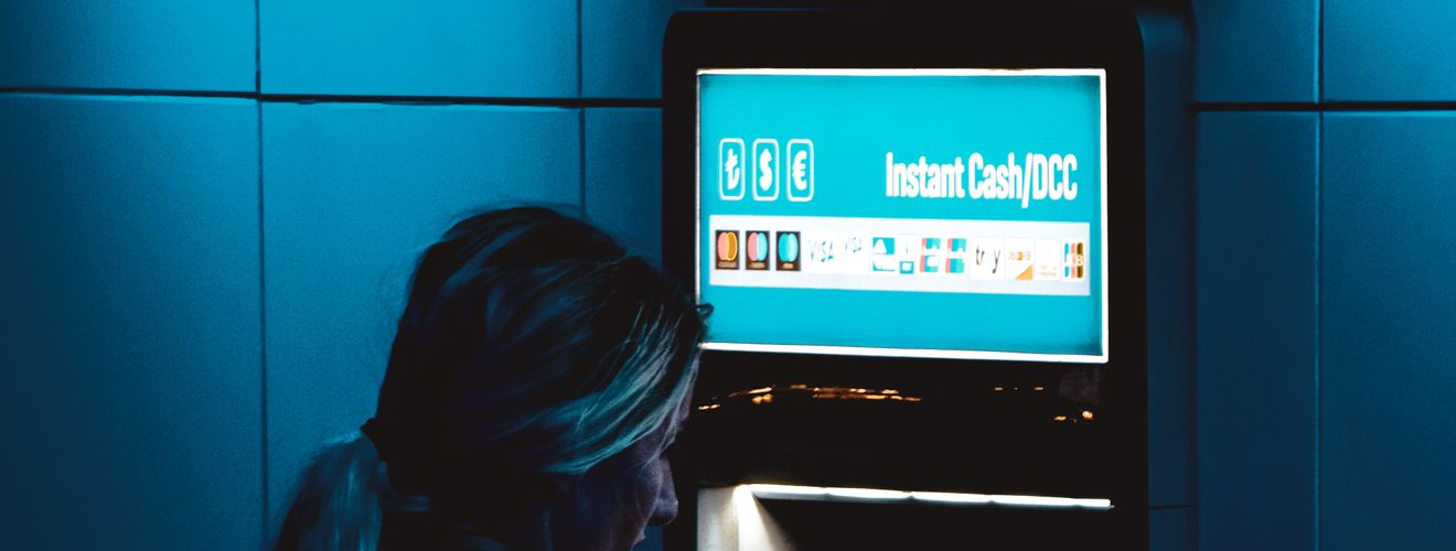 A woman uses an ATM at night in Istanbul under moody blue lighting.