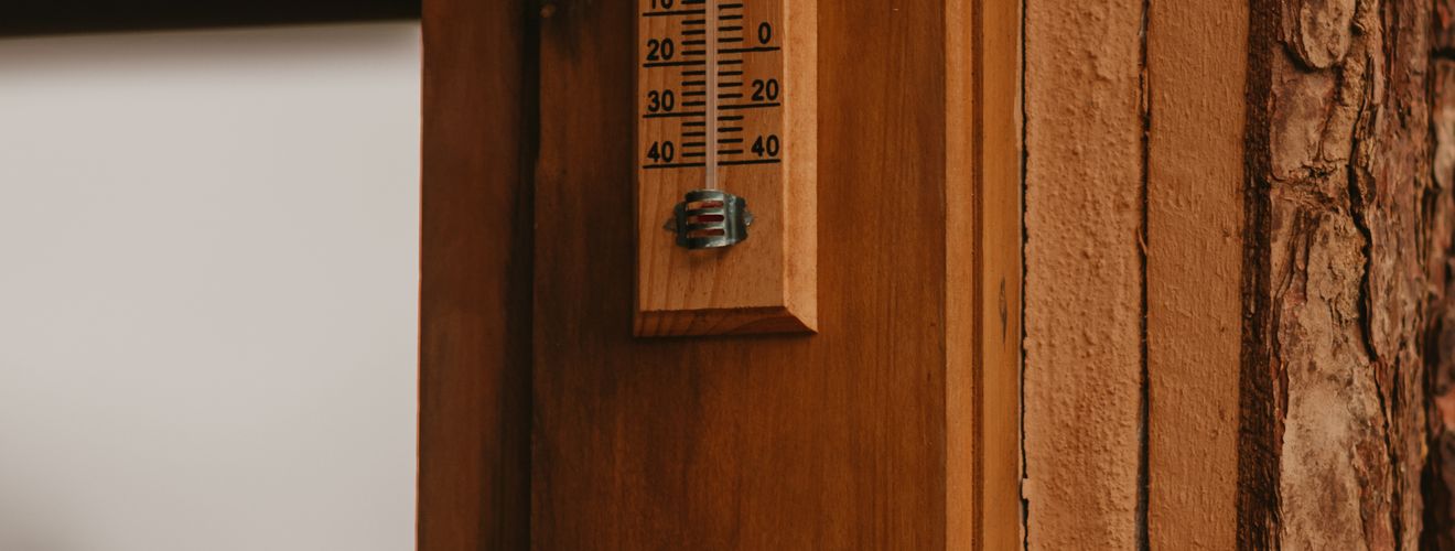 A wooden wall with a vintage thermometer displaying temperature in Celsius and Fahrenheit.