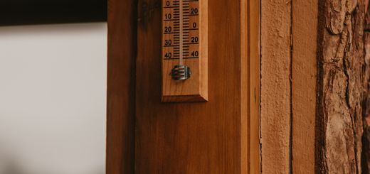 A wooden wall with a vintage thermometer displaying temperature in Celsius and Fahrenheit.