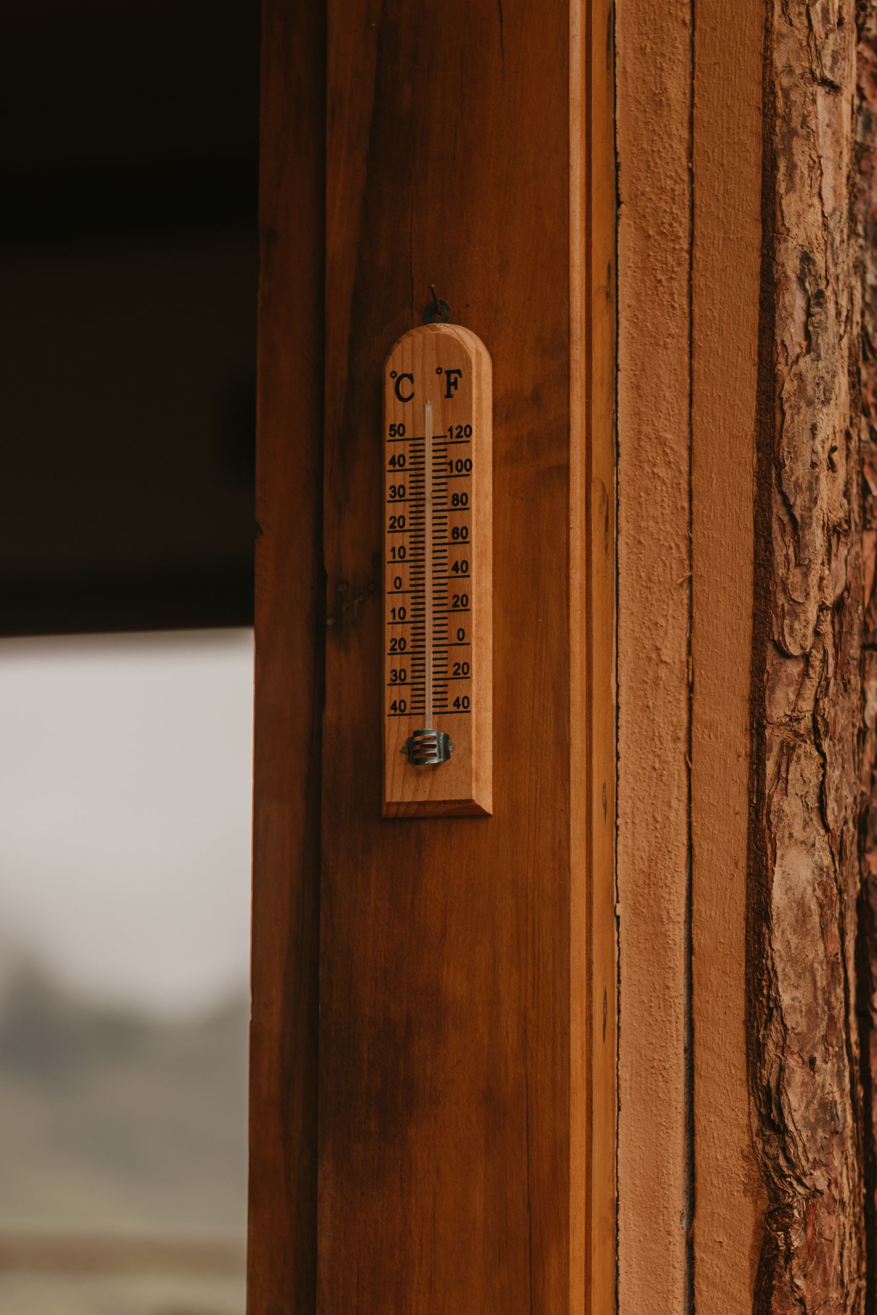 A wooden wall with a vintage thermometer displaying temperature in Celsius and Fahrenheit.