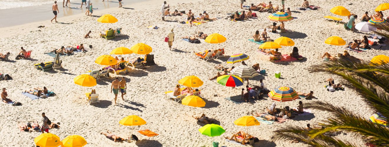 Aerial view of Clifton Beach with vibrant yellow umbrellas and beachgoers enjoying the sun and waves.
