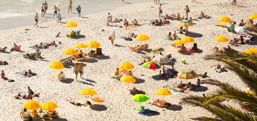 Aerial view of Clifton Beach with vibrant yellow umbrellas and beachgoers enjoying the sun and waves.