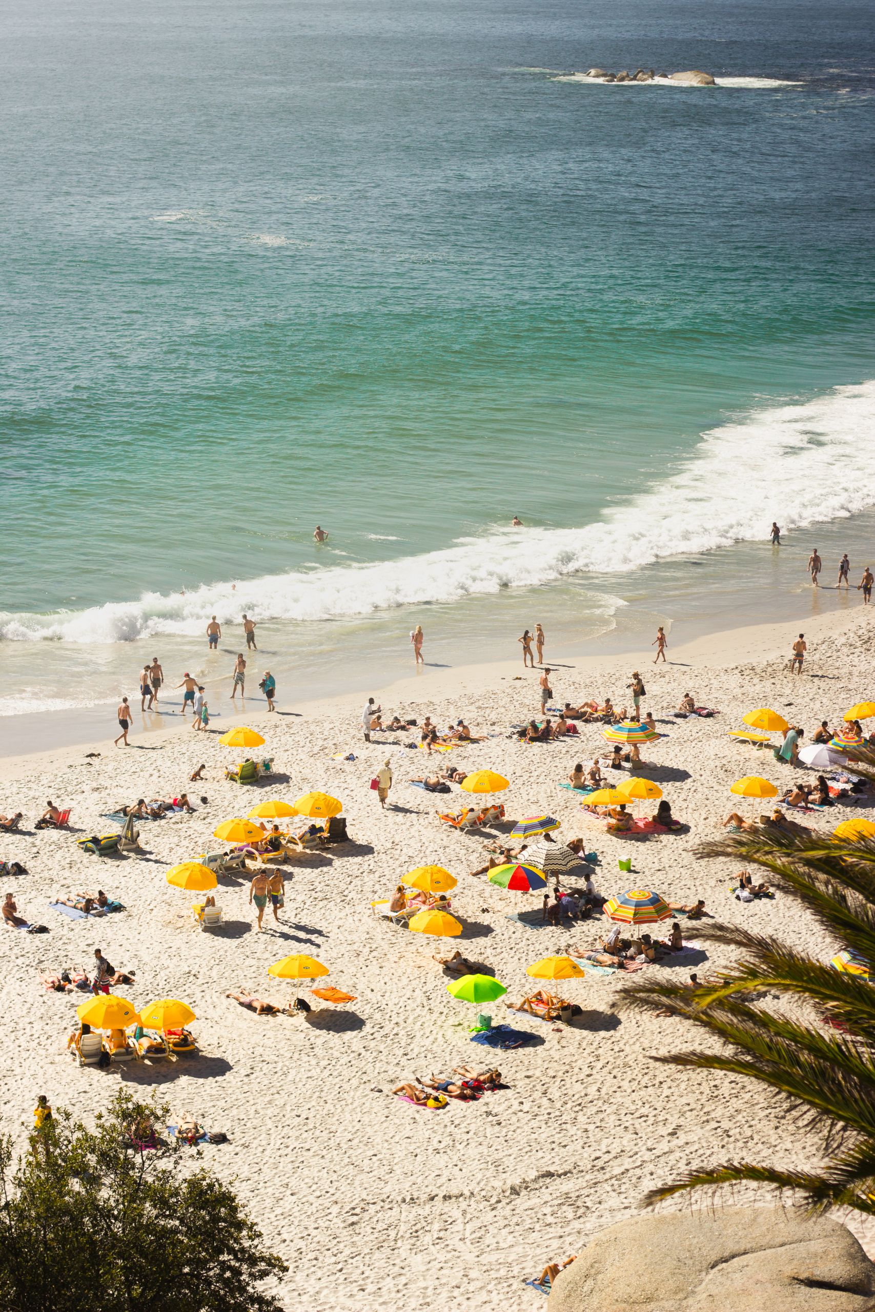 Aerial view of Clifton Beach with vibrant yellow umbrellas and beachgoers enjoying the sun and waves.