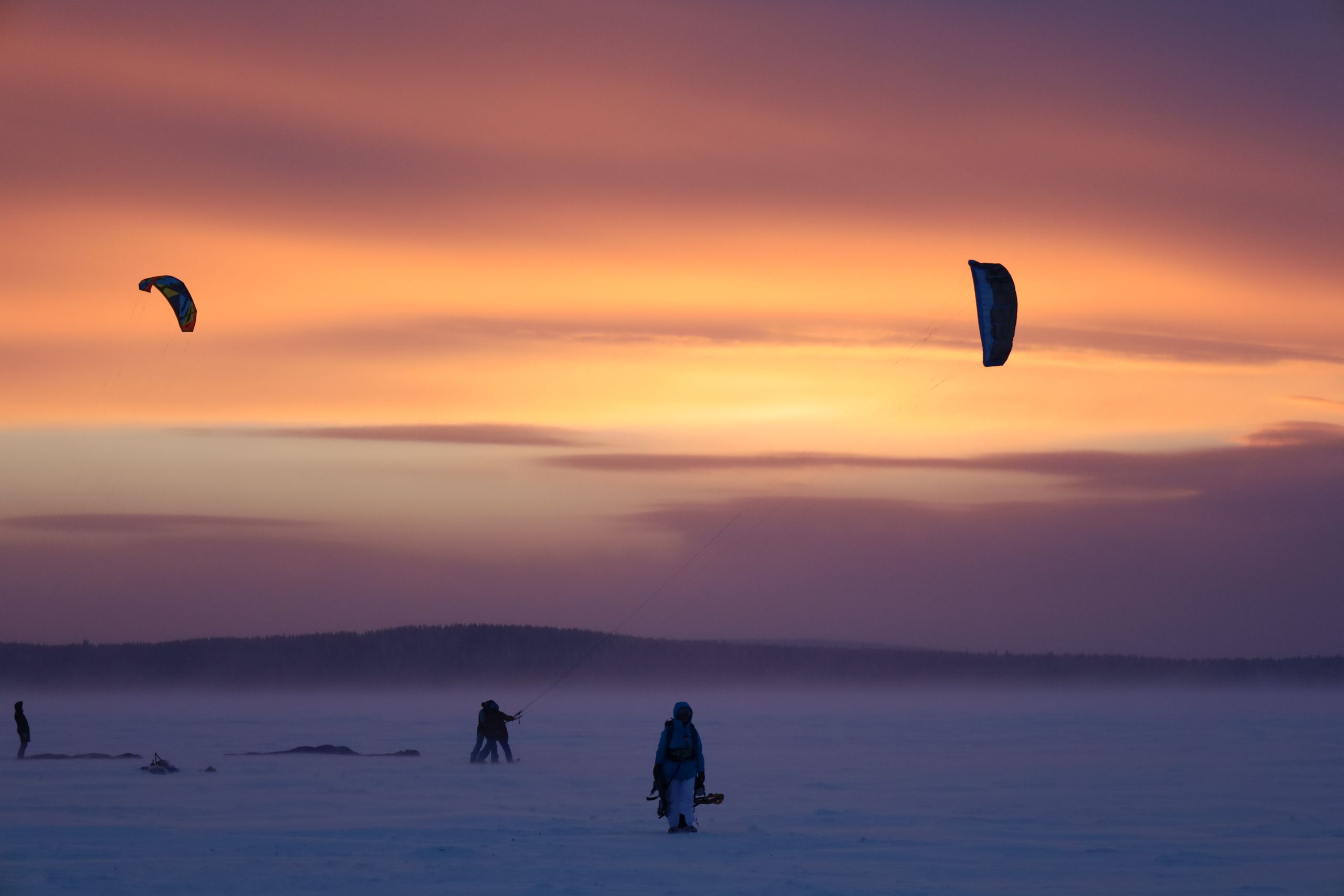 Captivating winter snowkiting scene with vibrant sunset skies and snowy landscape.