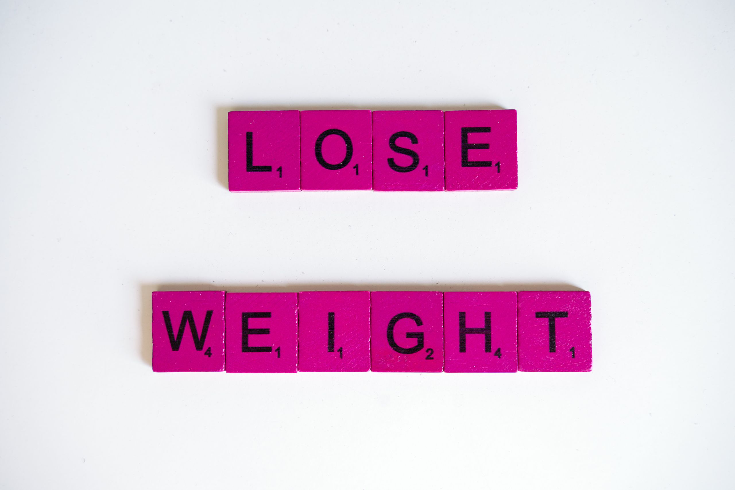 Creative image of the phrase 'Lose Weight' spelled with Scrabble tiles on a white background.