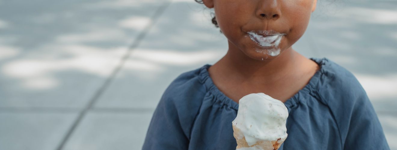 Crop anonymous ethnic kid with dirty mouth in casual clothes standing with ice cream in hands on street in daytime