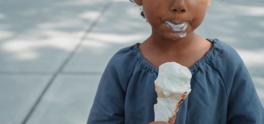 Crop anonymous ethnic kid with dirty mouth in casual clothes standing with ice cream in hands on street in daytime