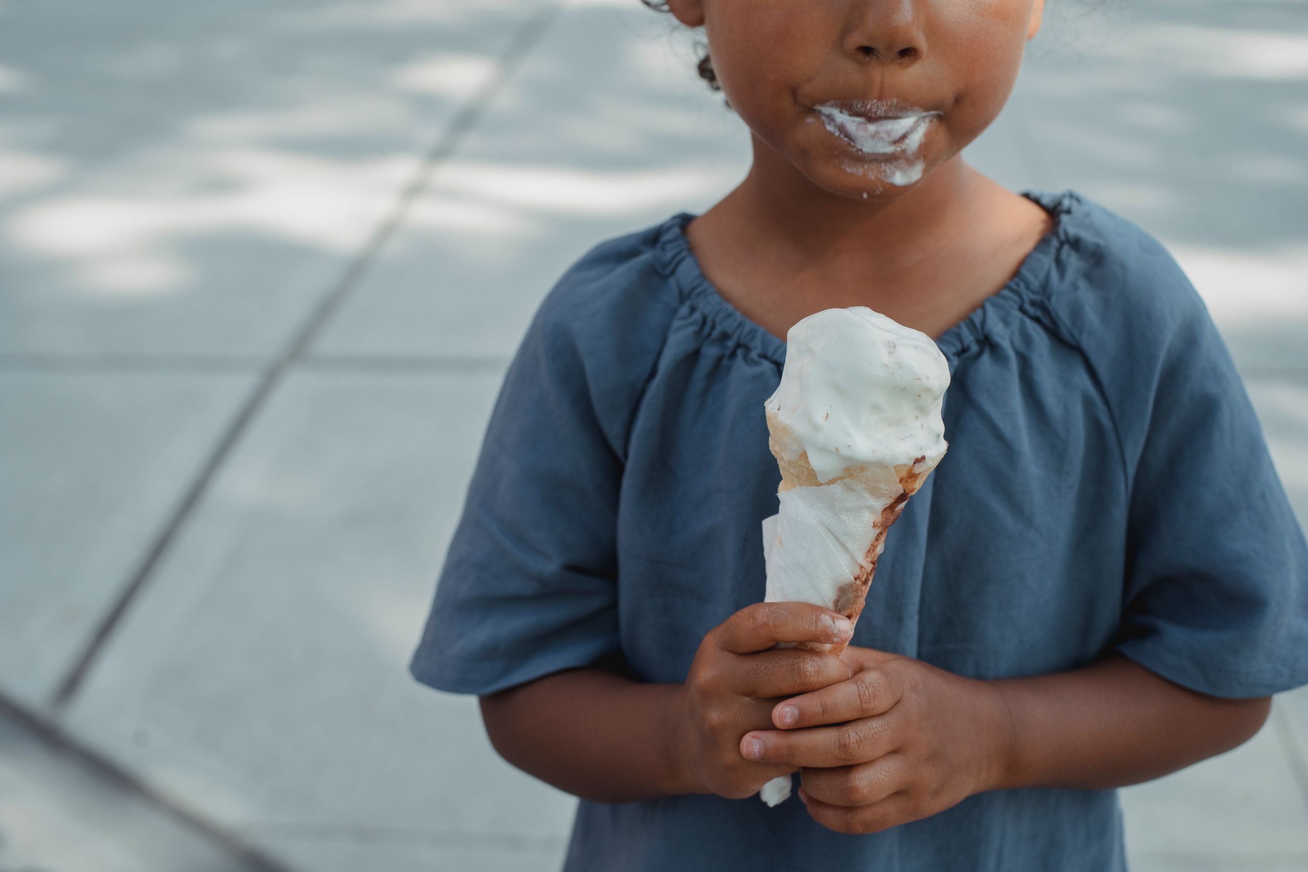 Crop anonymous ethnic kid with dirty mouth in casual clothes standing with ice cream in hands on street in daytime