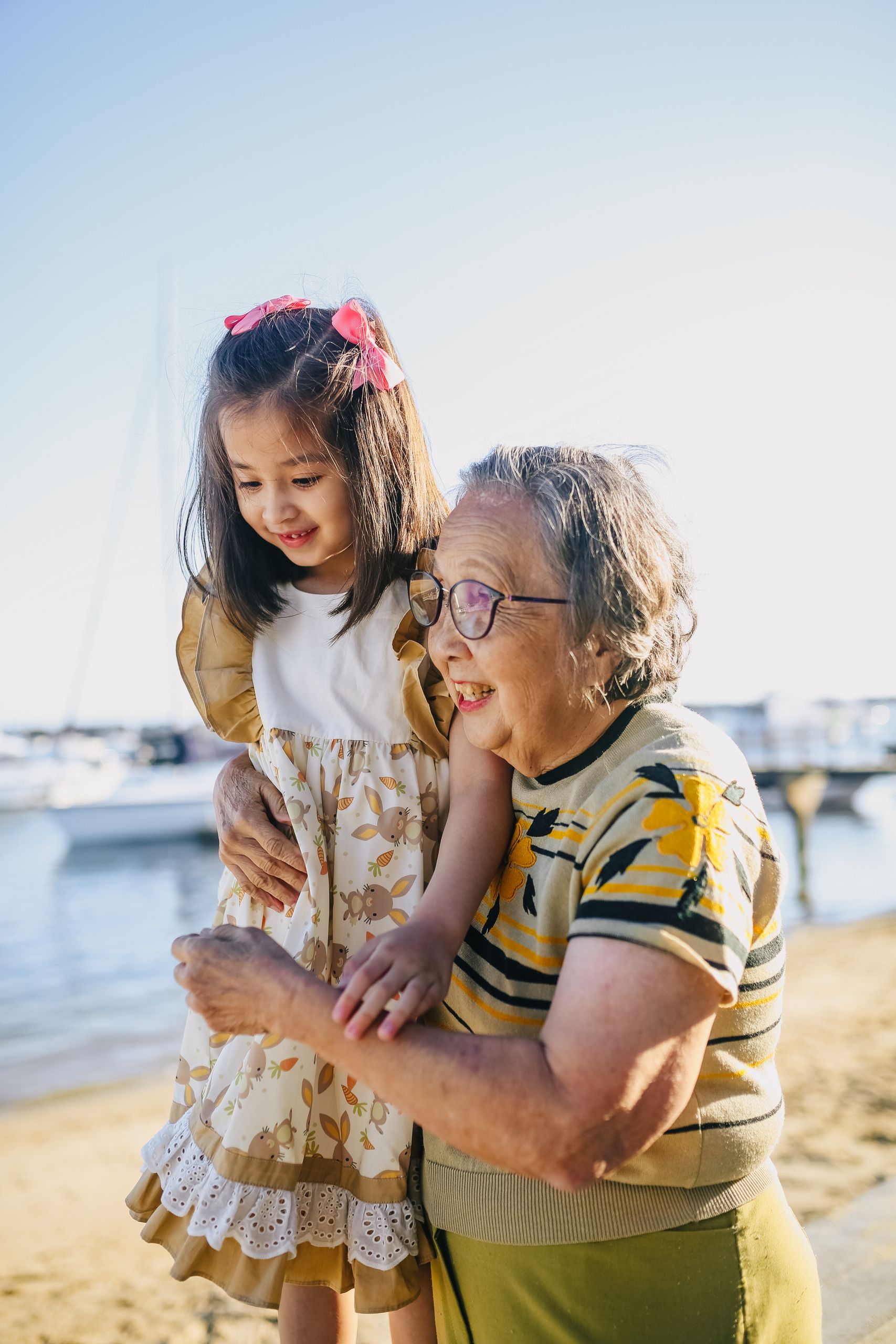 Happy Asian grandmother and granddaughter enjoying a sunny day at the beach, capturing joyful family moments.