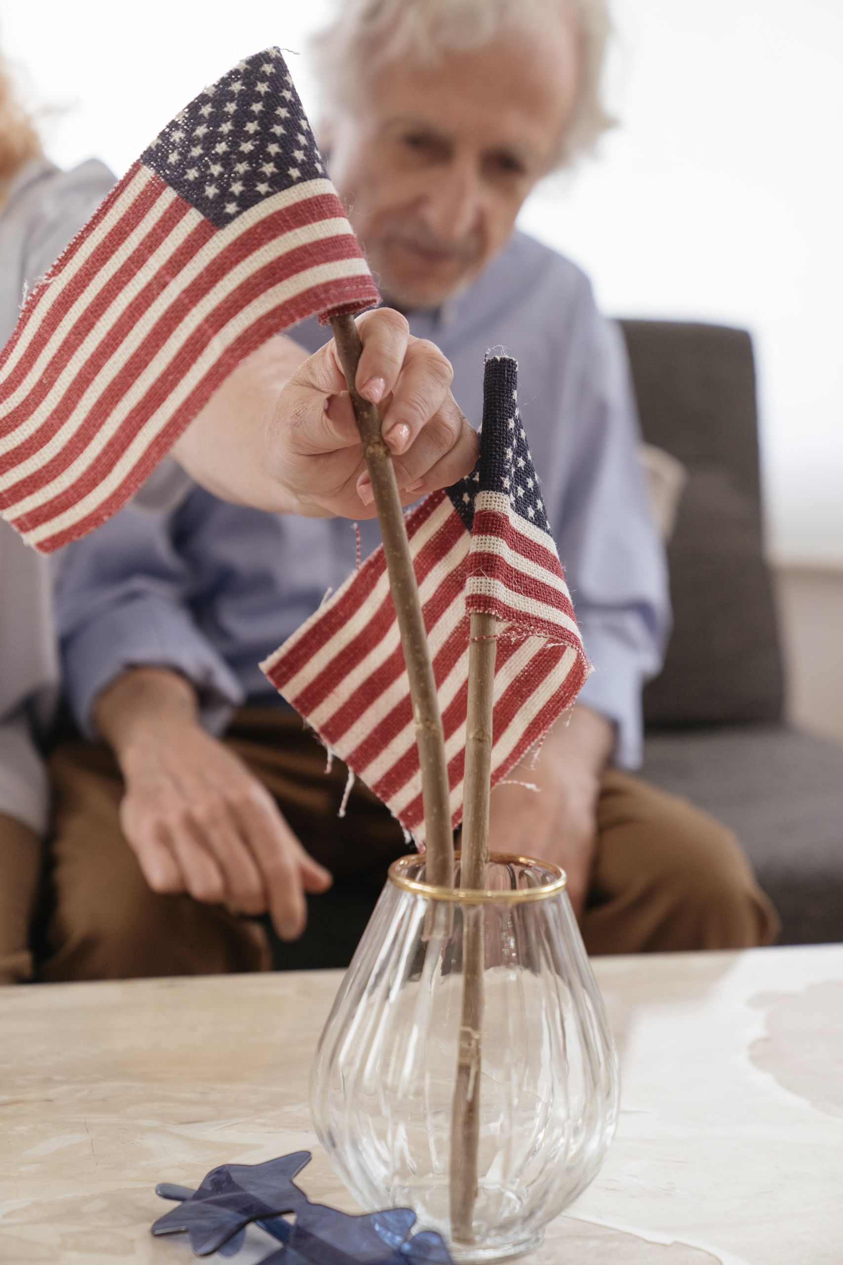Senior adult holding American flags in a vase, symbolizing patriotism and celebration.