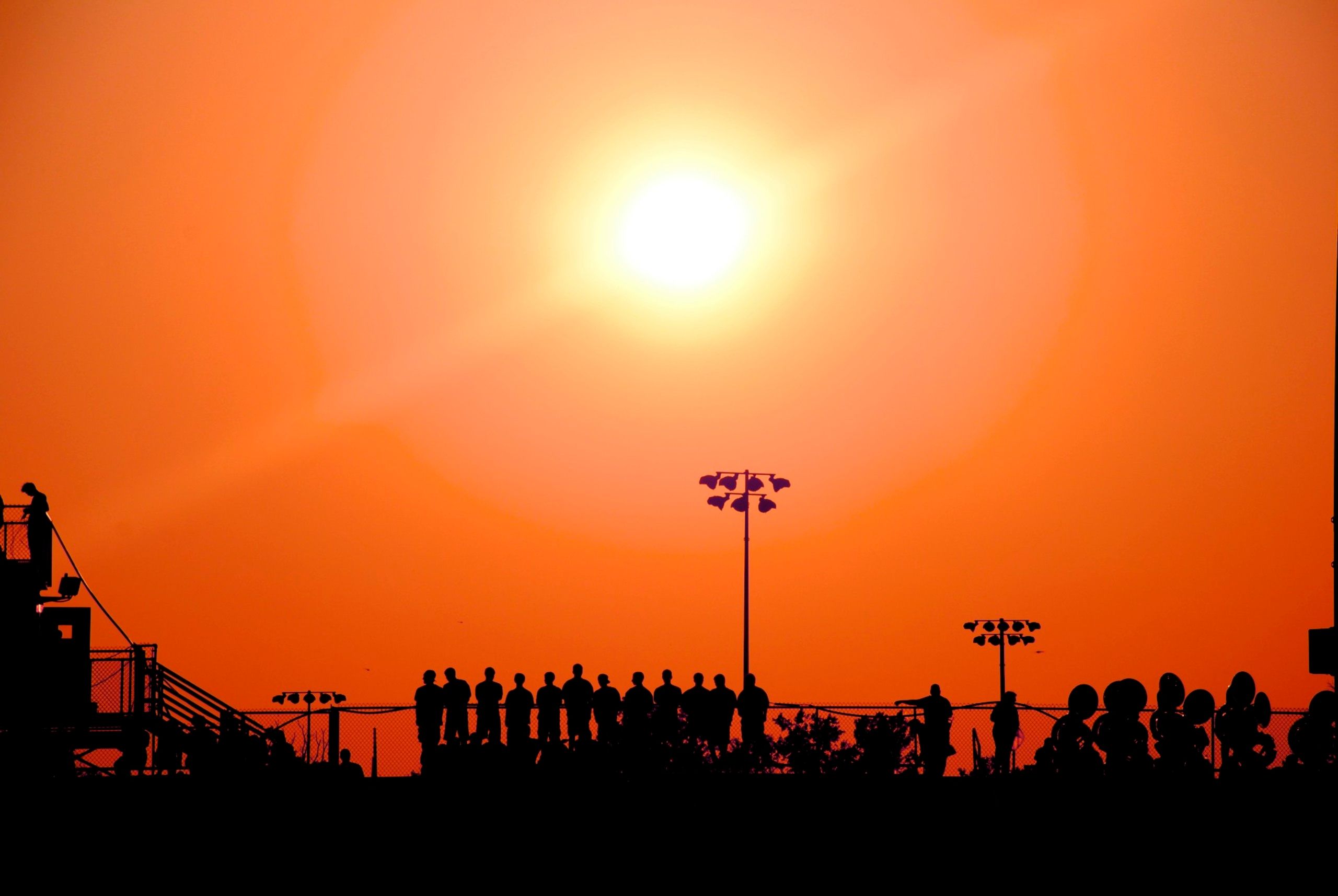Silhouetted crowd watching a sunset sports event with vivid orange sky.