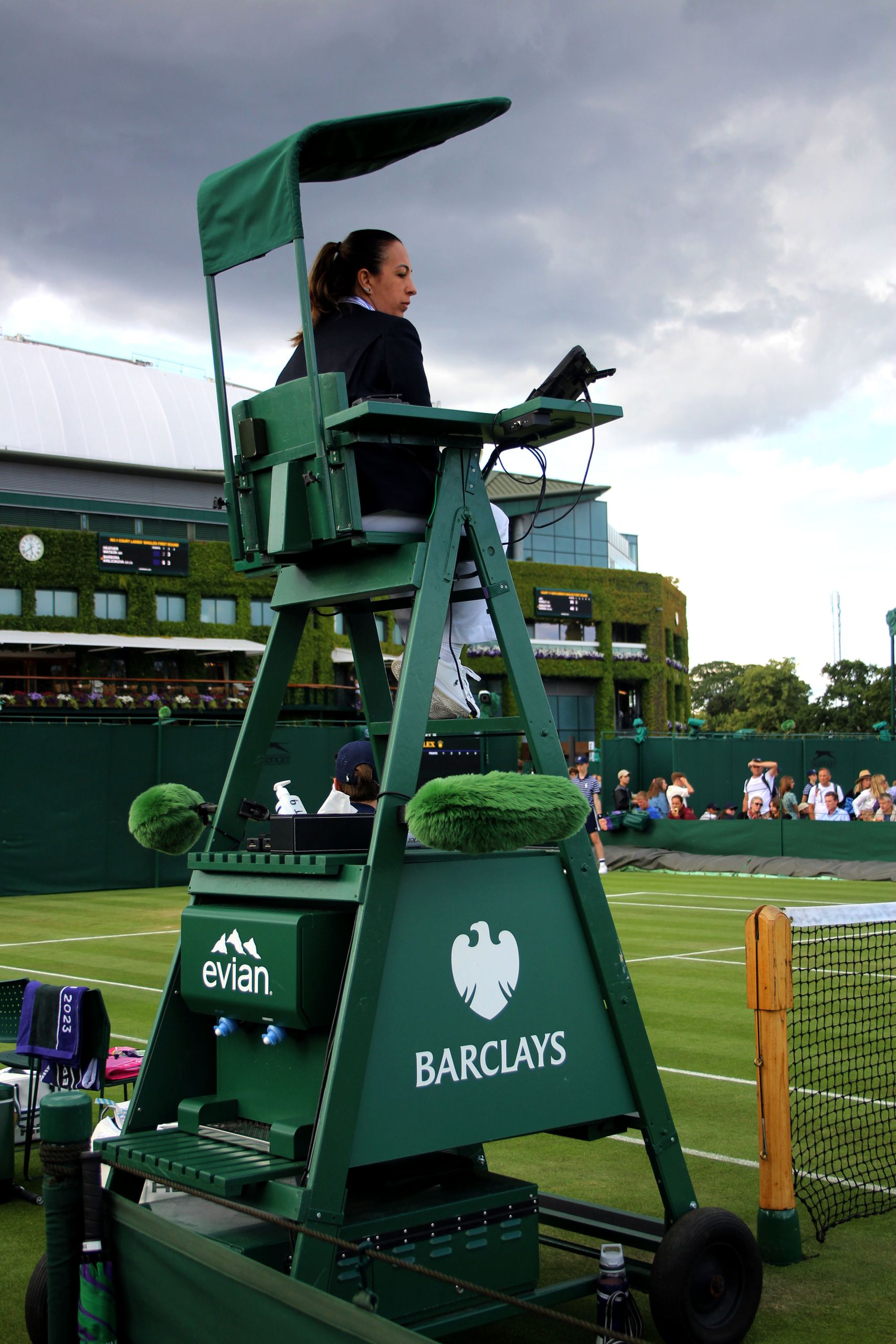 Tennis umpire seated in chair on outdoor court with Barclays sponsorship signage, evoking a competitive atmosphere.
