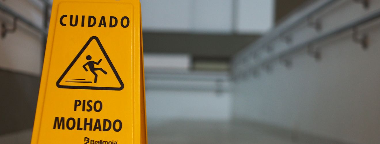 Yellow caution wet floor sign with Portuguese text in an indoor hallway.