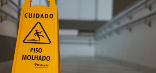 Yellow caution wet floor sign with Portuguese text in an indoor hallway.