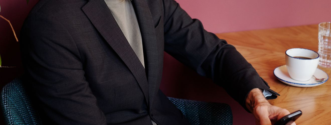 A mature man in a suit texts on his smartphone at a café table with coffee.
