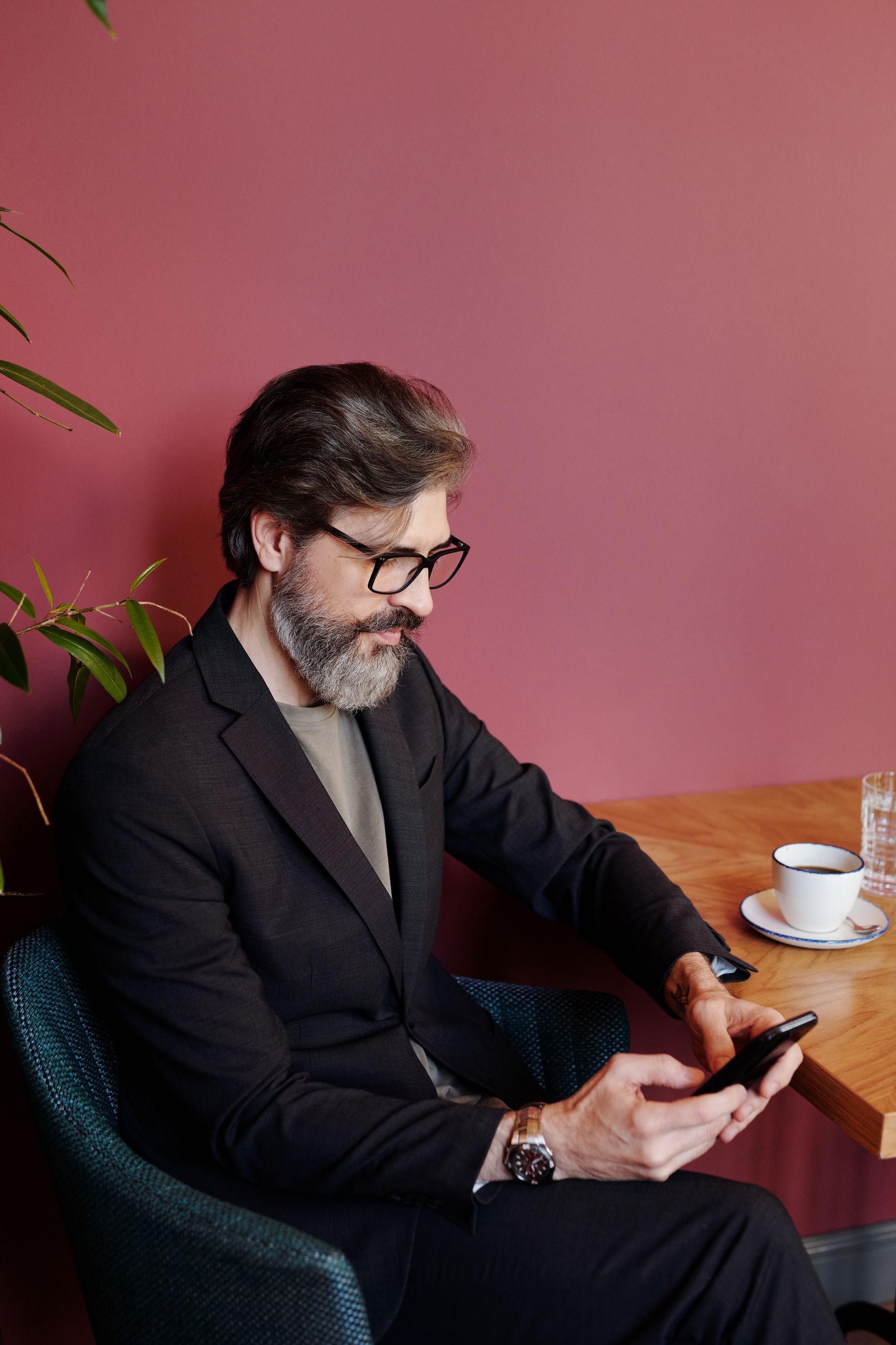 A mature man in a suit texts on his smartphone at a café table with coffee.