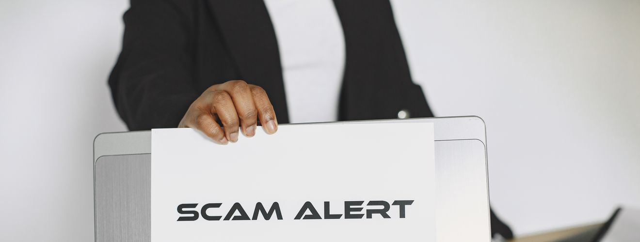 Business person holding a scam alert sign over a laptop, warning against online fraud.