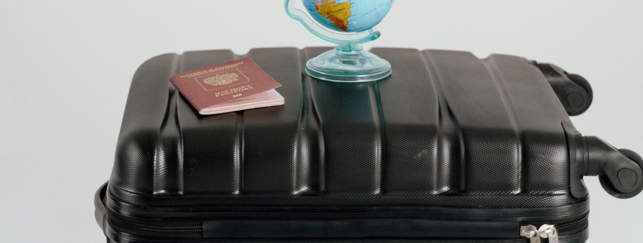 Creative travel concept featuring a cardboard sign, globe, passport, and suitcase against a white background.