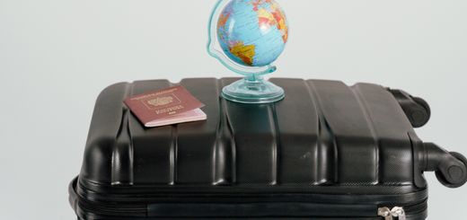 Creative travel concept featuring a cardboard sign, globe, passport, and suitcase against a white background.