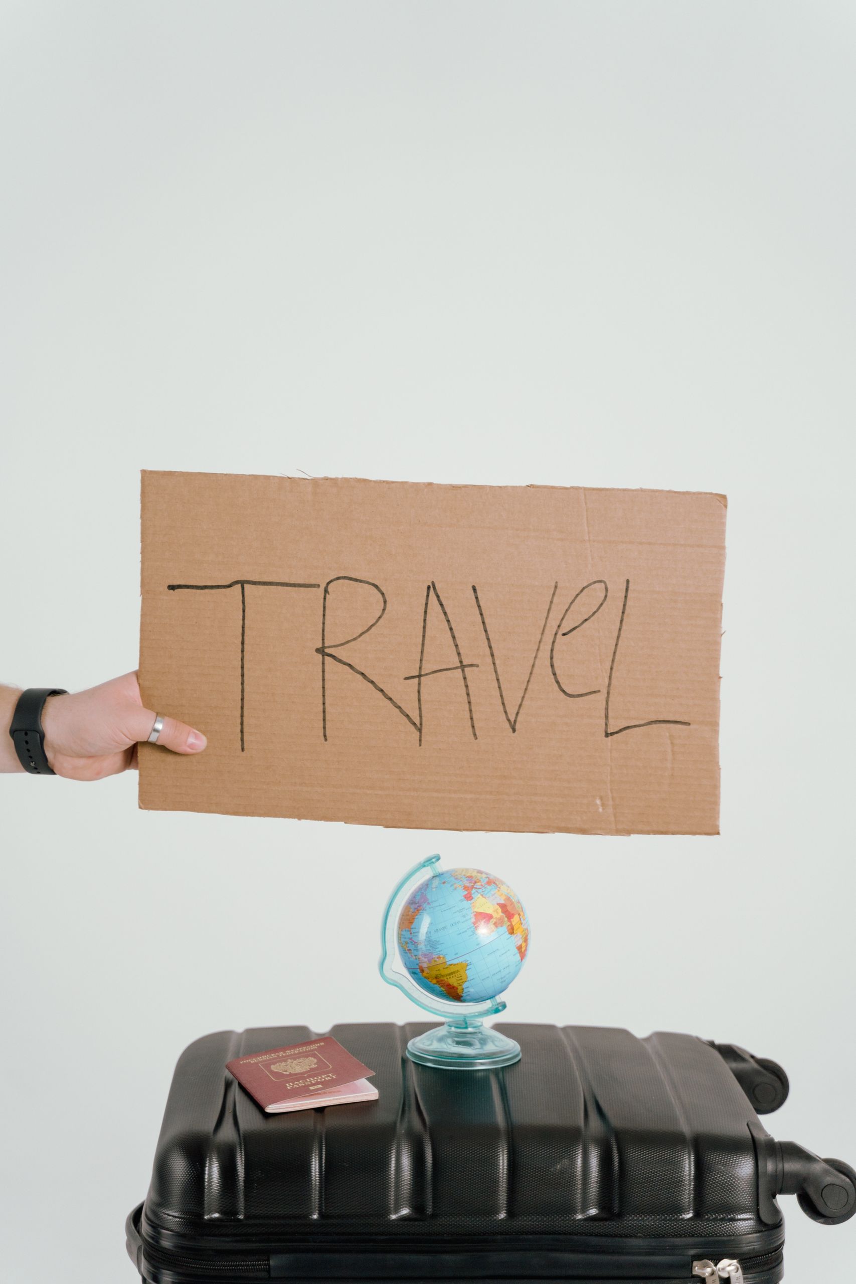 Creative travel concept featuring a cardboard sign, globe, passport, and suitcase against a white background.