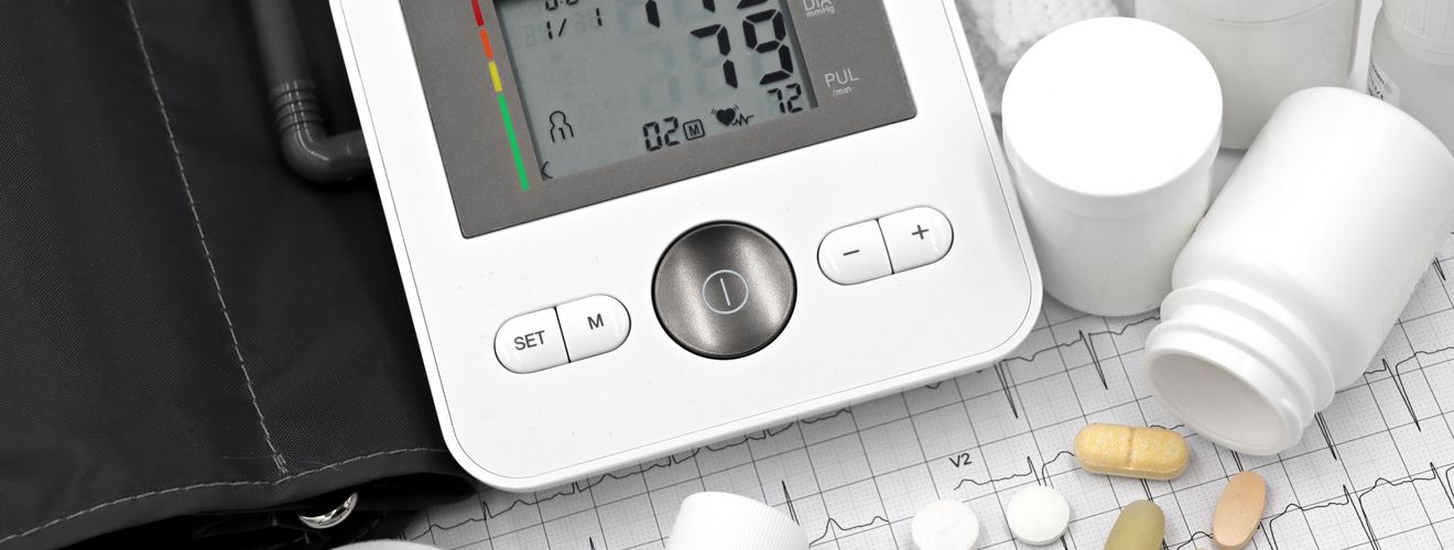 Digital blood pressure monitor on ECG paper with pills and medical supplies, ideal for healthcare topics.