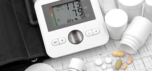 Digital blood pressure monitor on ECG paper with pills and medical supplies, ideal for healthcare topics.