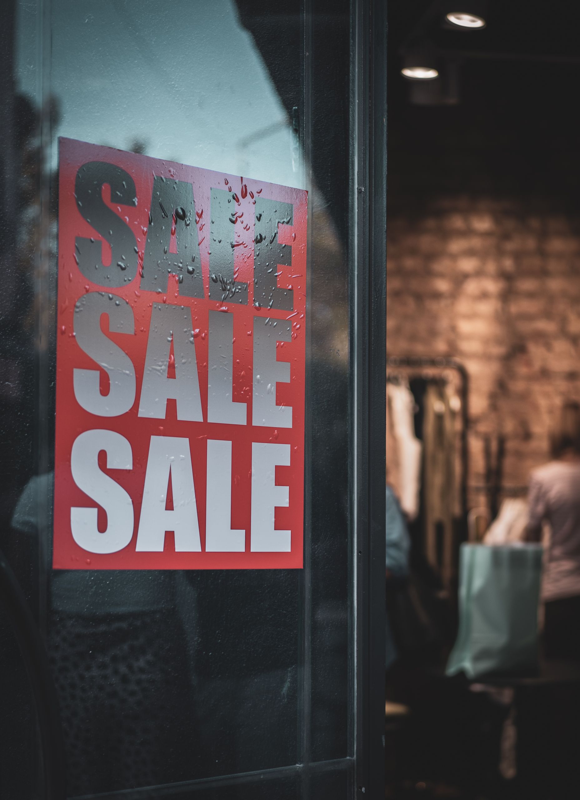 Red sale sign on a glass door with interior view of a clothing store.