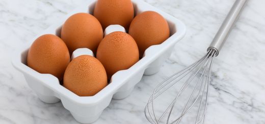 Six brown eggs in a carton and a metal whisk on a marble countertop. Perfect for cooking concepts.