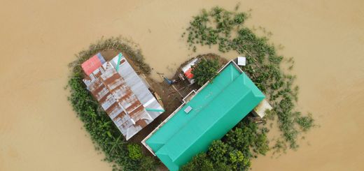 Top-down view of a flood-affected area in Bangladesh showing buildings and surrounding submerged land.